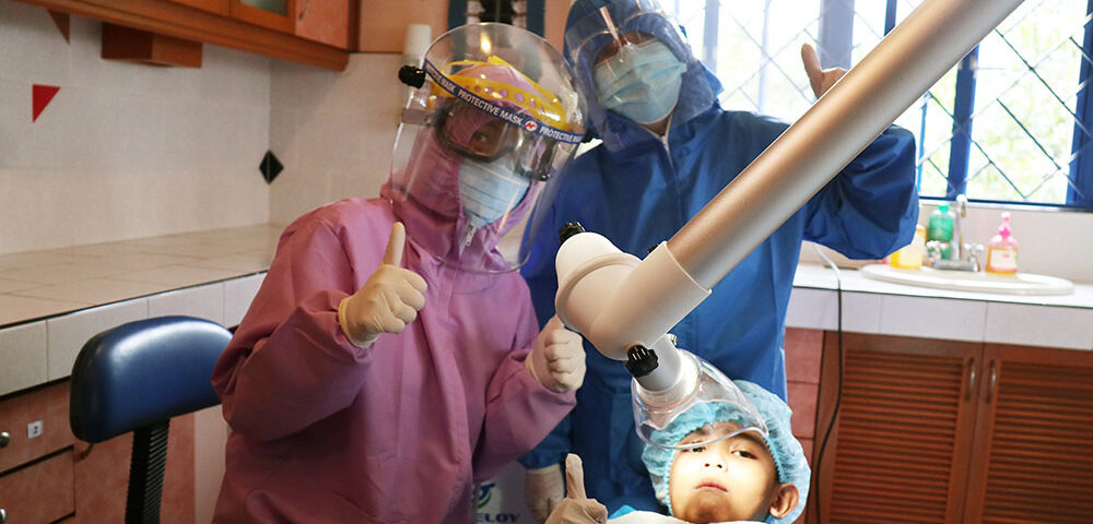 Our dentist, Dr. Vanessa in pink PPE suit, her assistant, and her patient